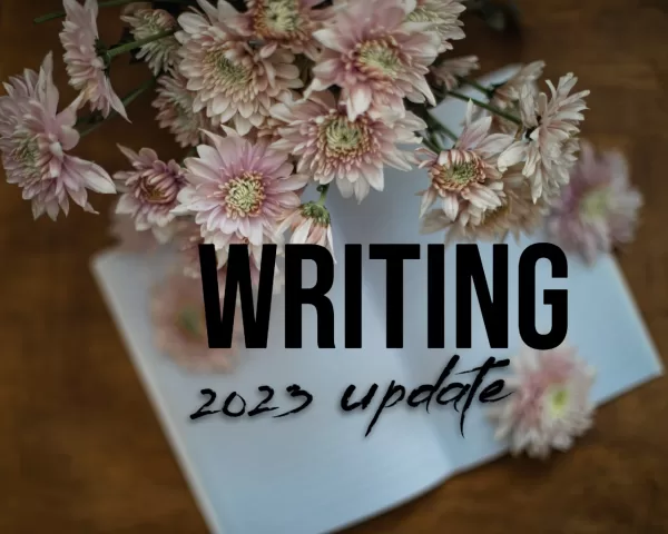 pink flowers on white blank notebook with the words "writing: 2023 update" 